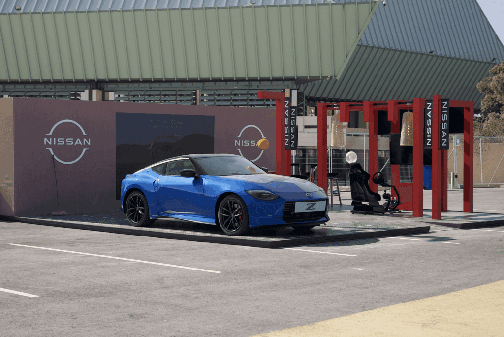 A blue Nissan Z sports car showcased at a display with red structures and a Nissan logo, featuring image.