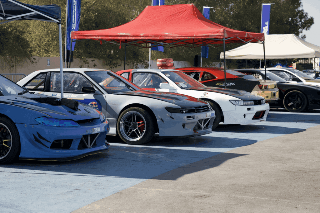 A lineup of colorful drift cars under a red tent, showcasing image.