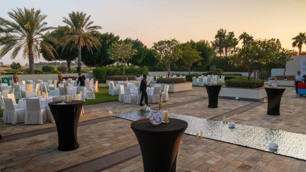 An outdoor event setting with tables and palm trees at sunset, showcasing image.