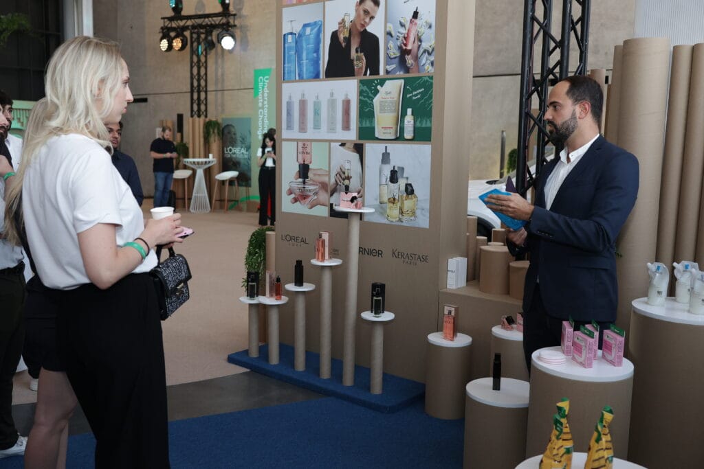 A L'Oreal product presentation event with a woman holding a coffee cup and a presenter discussing beauty products, showcasing image.