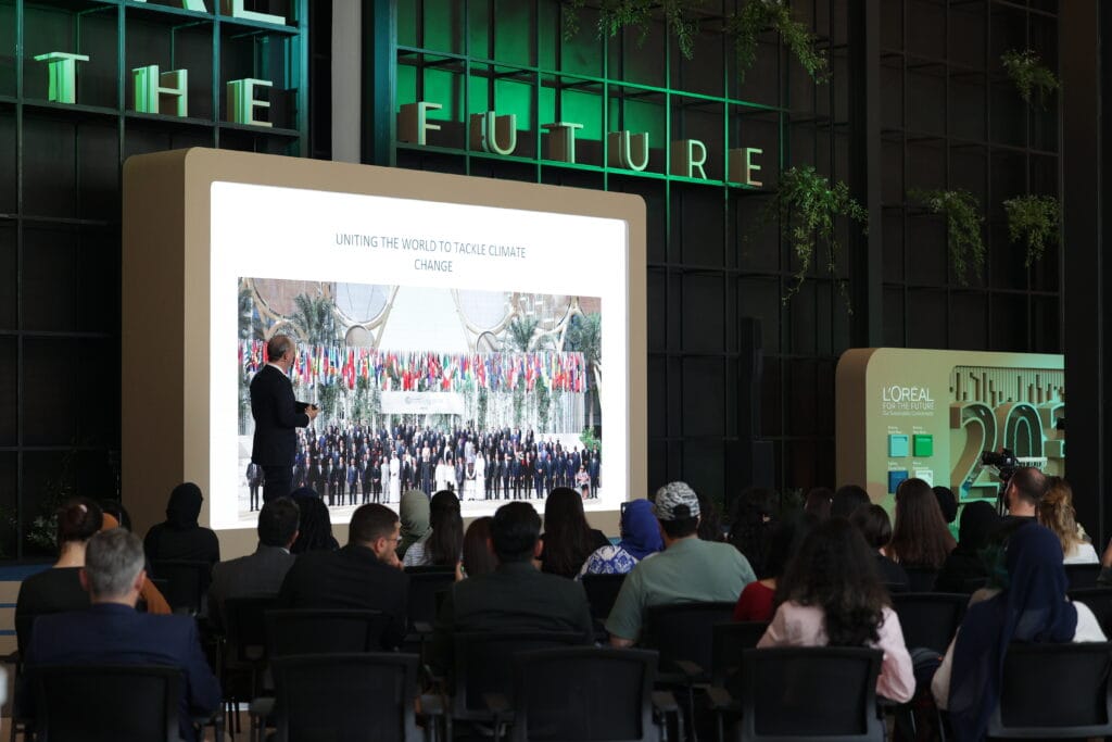 A speaker presenting at a climate change conference with a large screen displaying a group photo, emphasizing image.