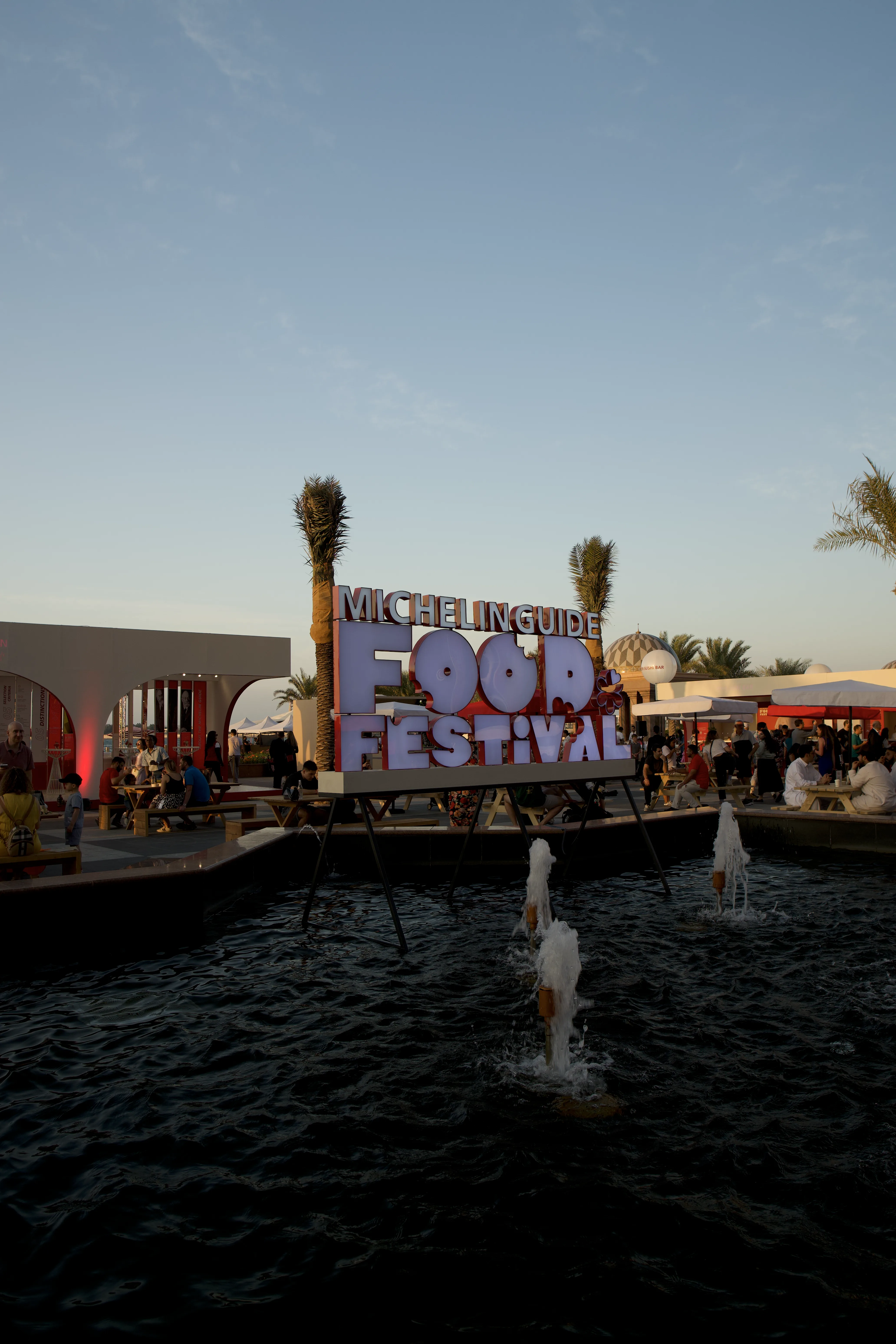 A vibrant sign for the Michelin Guide Food Festival near a water fountain, showcasing image.
