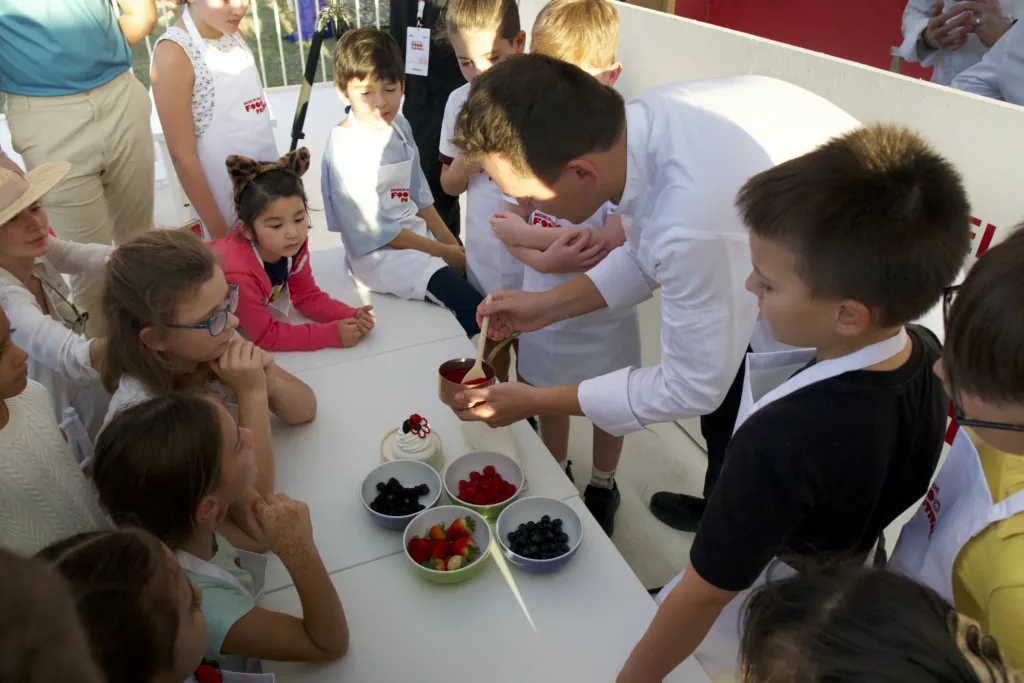 A chef demonstrating dessert preparation to children in a cooking class, showcasing image.