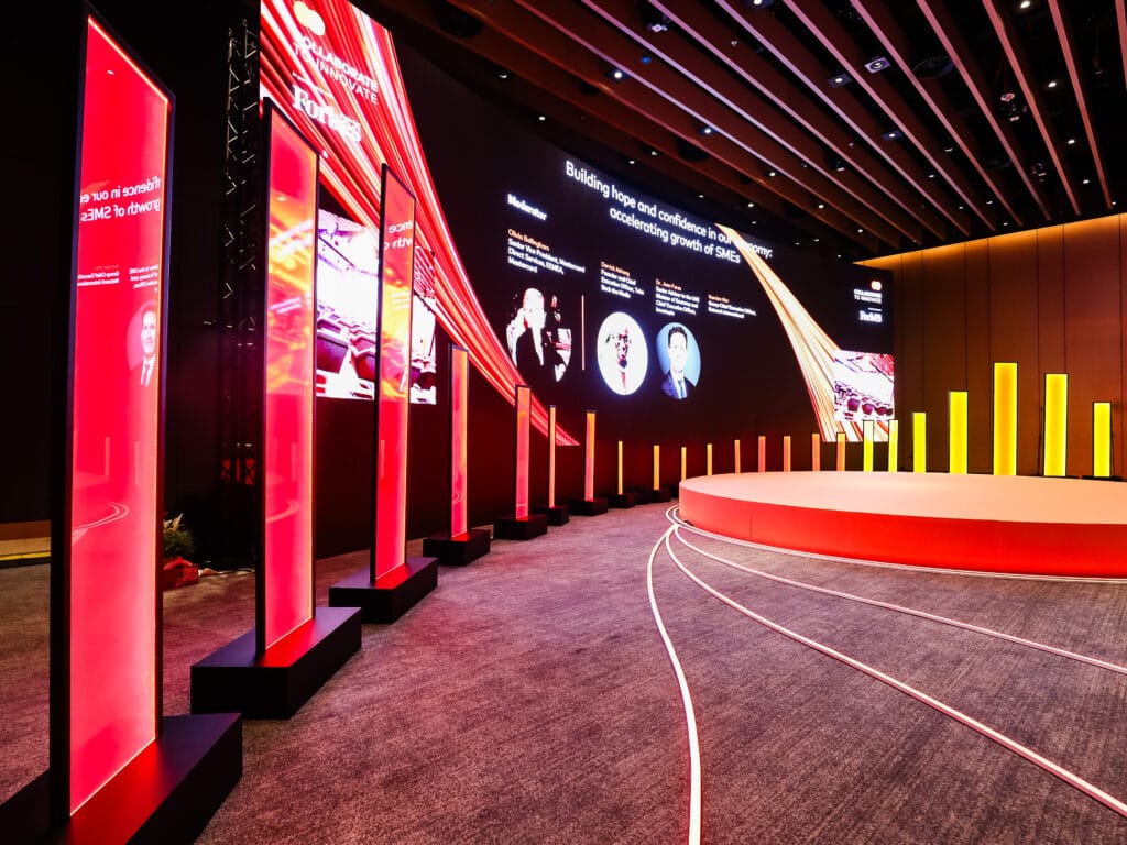 A modern event stage with red lighting and digital displays, showcasing image.