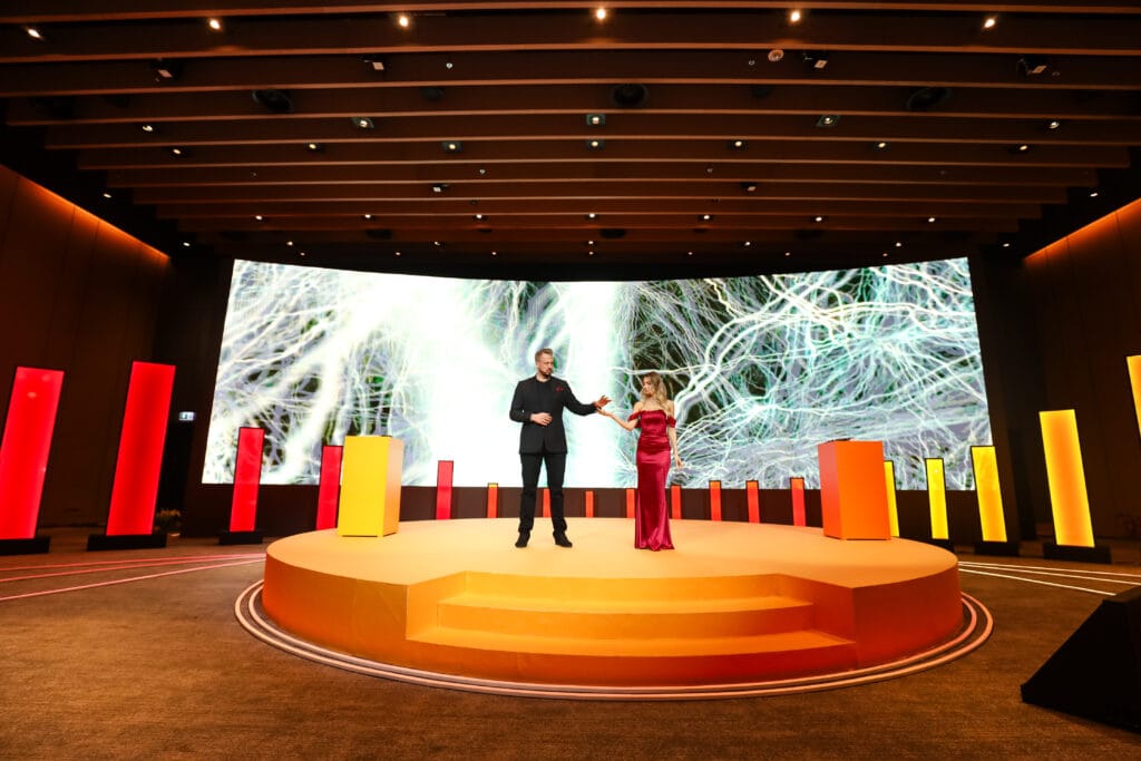 A stage presentation featuring a man in a black suit and a woman in a red dress, highlighting image.
