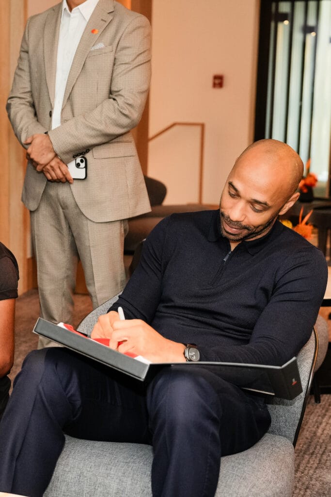 A man in a navy sweater signing a book while seated in a modern interior, showcasing image.