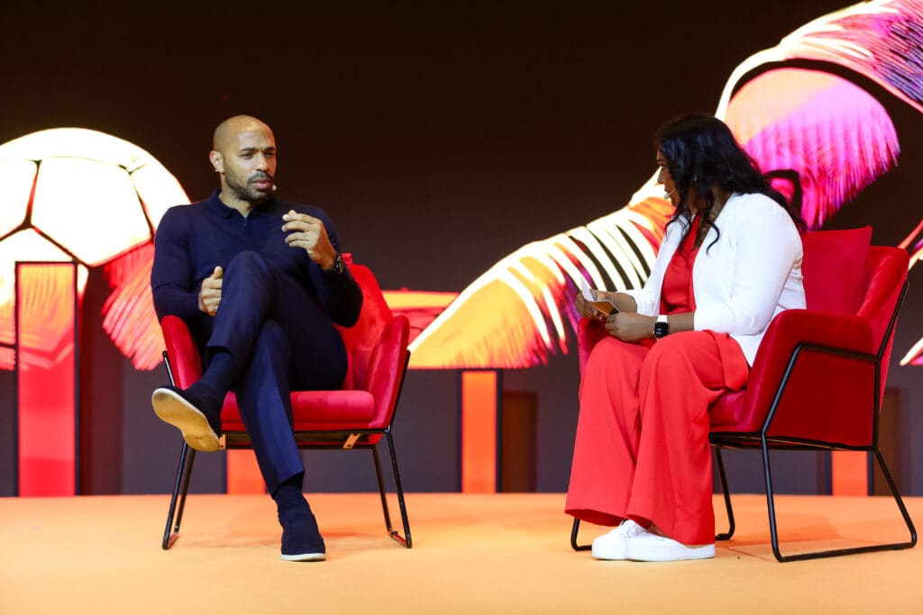 Thierry Henry seated in a red chair during an interview, discussing soccer, showcasing image.