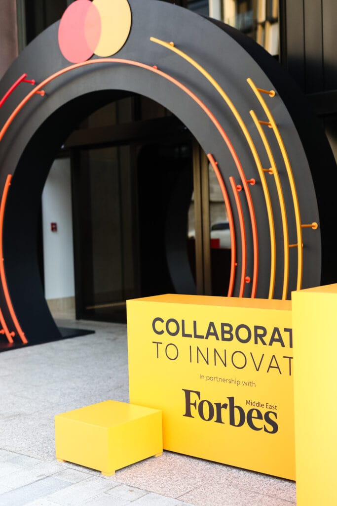 A vibrant yellow box displaying 'COLLABORATE TO INNOVATE' at a Forbes event, featuring a colorful arch.